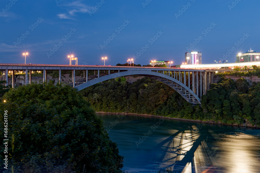 Fototapeta premium Rainbow Bridge at night illuminated with city lights, view from Canadian side, Niagara Falls