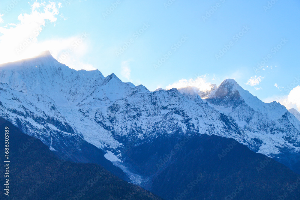 Fototapeta premium Jagged, snowy peaks loom under a cloudy sky Yala Snow Mountain, Sichuan, China