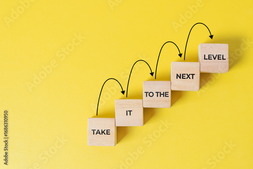 Business career path for growth and success concept. Wooden block ladder with the message take it to the next level with stepping up arrows