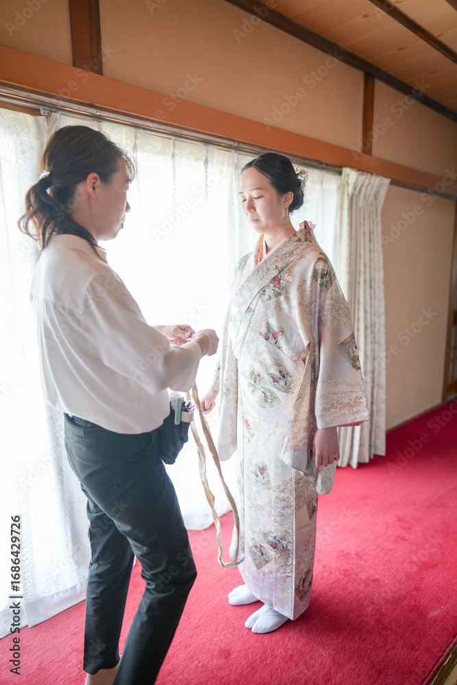 Fototapeta premium A woman in a kimono is being helped by another woman. The woman in the kimono is wearing a white shirt and black pants