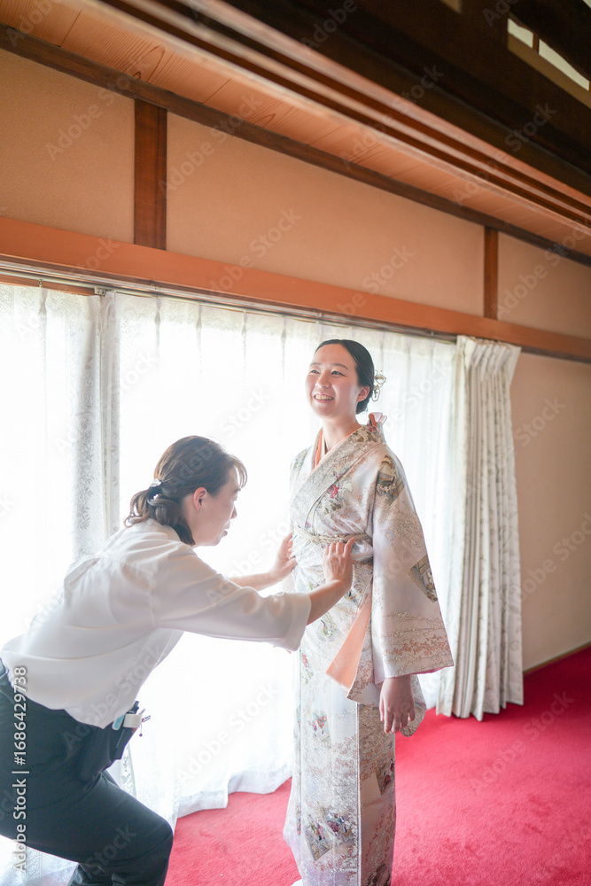 Obraz premium A woman is getting dressed in a kimono with a man helping her. The woman is smiling and she is happy