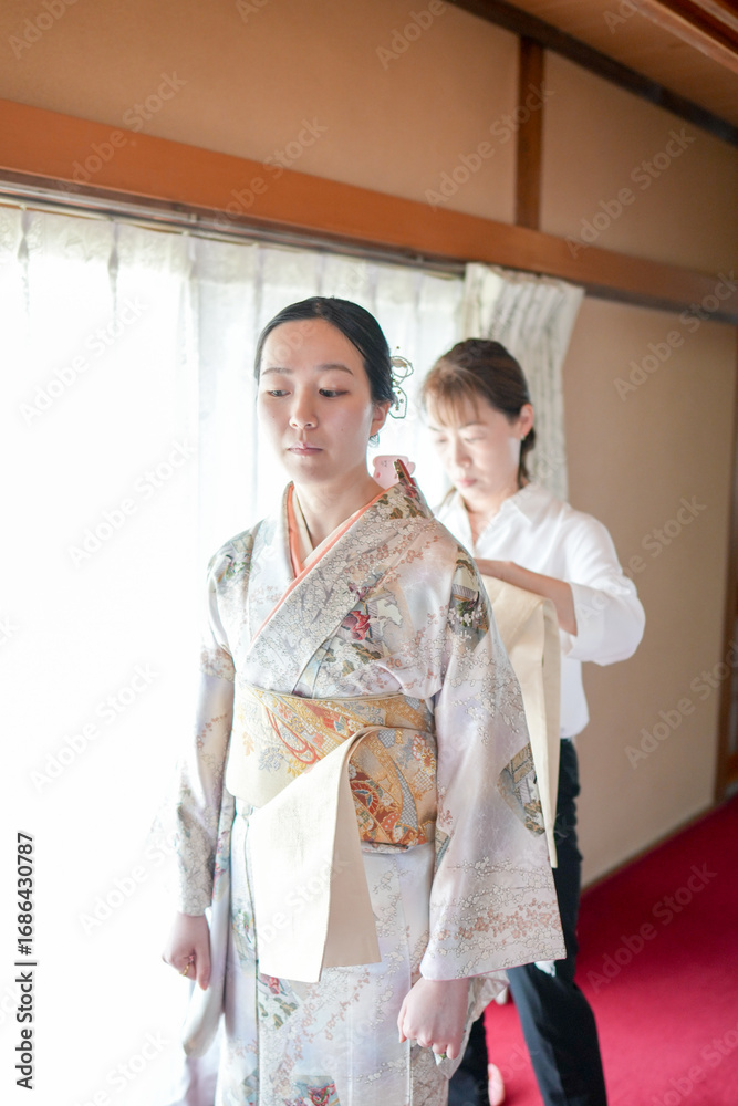 Fototapeta premium A woman in a kimono is being helped by another woman. The woman in the kimono is wearing a white shirt underneath her kimono
