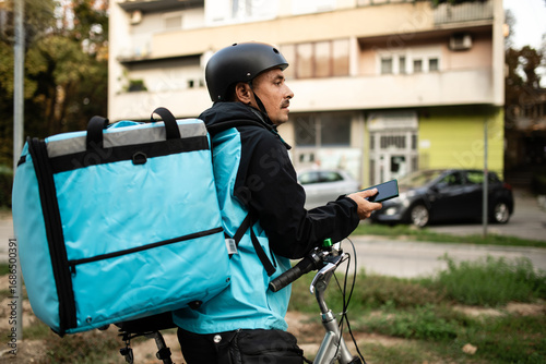 Photos Deliveryman using smartphone and carrying thermal backpack riding bicycle
