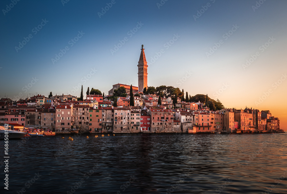Fototapeta premium Rovinj, Croatia - Sunset view of beautiful Old Town of Rovinj with the tower of Saint Euphemia church in Adriatic sea coast. Clear blue sky, golden sunset colours