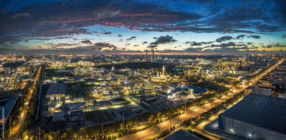 Fototapeta premium Panoramic view of a sprawling industrial zone with an illuminated chemical plant under a colorful twilight sky.