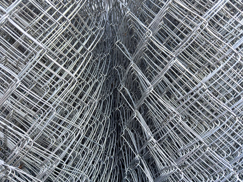 Closeup of stacked metal wire mesh rolls, showing geometric pattern of galvanized steel fence material used in construction and protection.
