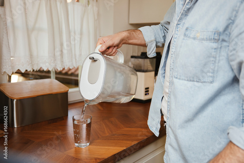Person pouring filtered water from jug into glass in kitchen