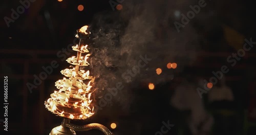 Varanasi, India. Man makes movements with a candle holder with lit candles on the Ganga Maha Aarti ceremony begins. Brahman priest wearing red and yellow dress doing traditional ganga aarti at ghat