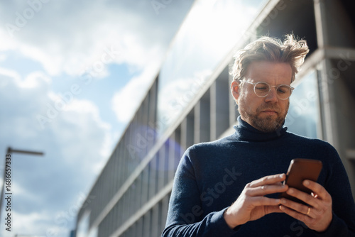 Businessman with eyeglasses using mobile phone on sunny day