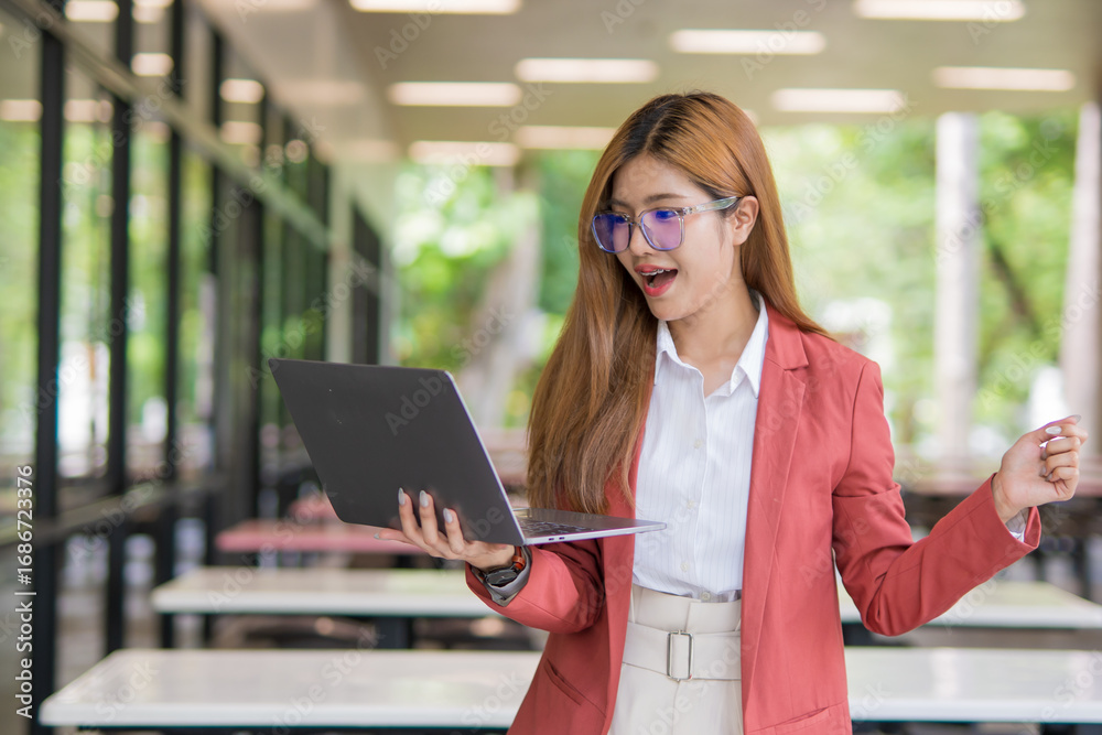 Fototapeta premium Asian businesswoman using digital laptop while standing in front of modern building. Attractive female employee working in front of office.