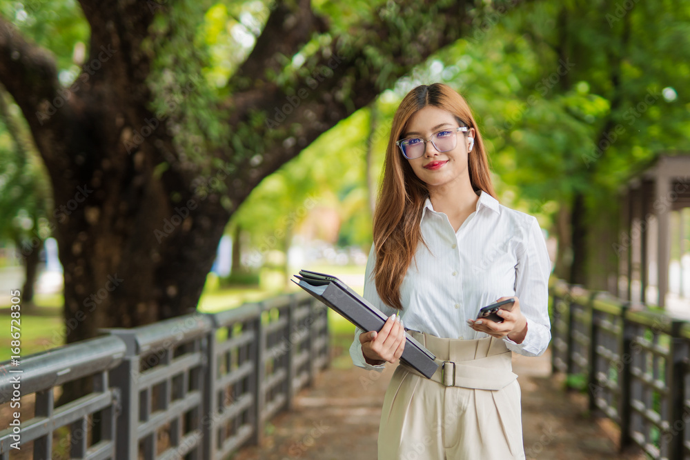 Naklejka premium Asian female student in warm clothes using phone to chat with friends and ready for video call while in university.