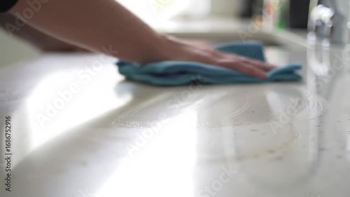 Hand cleaning white kitchen countertop with blue microfiber cloth with closeup.