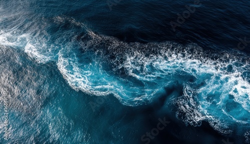 Bright sunlight reflects on the tranquil ocean as waves gently lap at the surface, creating a stunning interplay of blues and whites near the shoreline. The calmness of the scene evokes peace
