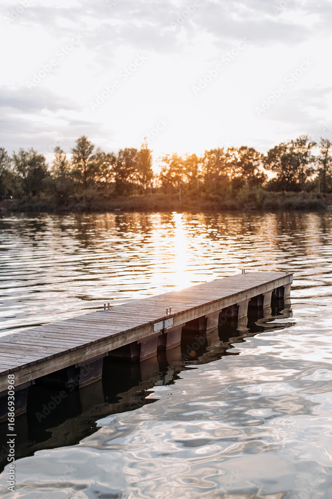 Naklejka premium Sunset view over tranquil lake with wooden dock and reflections in the water