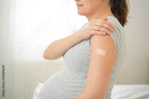 Expecting mother arm with fresh vaccination bandage. Important step in scheduled prenatal immunization program.