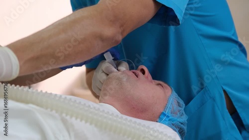 Surgeons and nurses are preparing and inserting an endotracheal tube into a patient's trachea to ensure proper ventilation during a surgical procedure inside a hospital operating room
