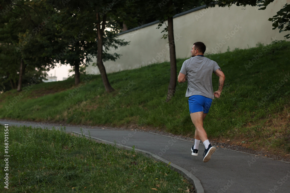 Obraz premium Athletic young man in sportswear running outdoors, back view. Space for text