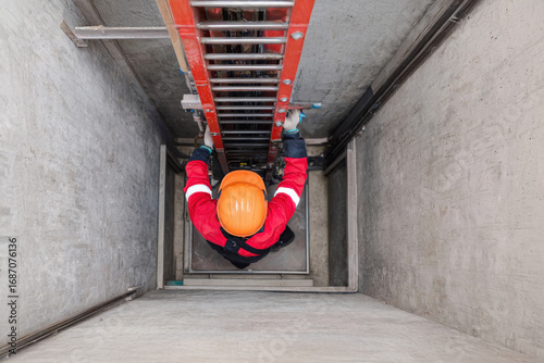 Worker in yellow helmet standing in front of closed elevator doors in modern building.