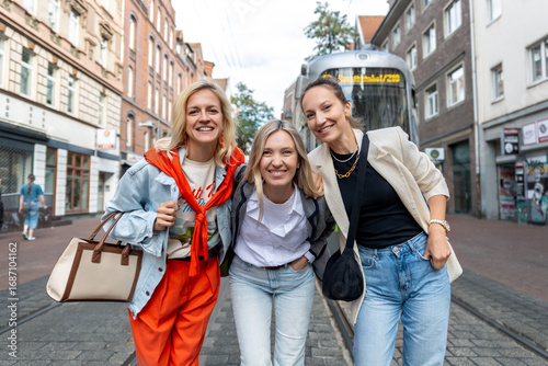 Bild auf Leinwand Three cheerful young adult women friend walk street old european german Hannover city street enjoy having fun laughing sunny day together