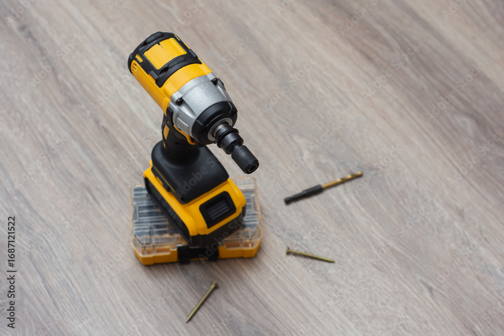 Fototapeta premium Cordless impact wrench on a wooden surface, accompanied by screws, drill bits, and a storage case. Electric tools for construction and DIY projects.