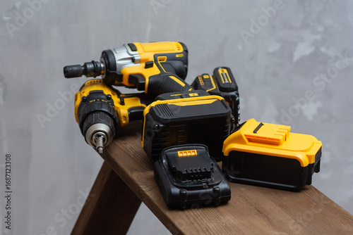 Professional cordless power tool set with yellow and black drill, impact driver, and lithium-ion batteries on wooden surface.