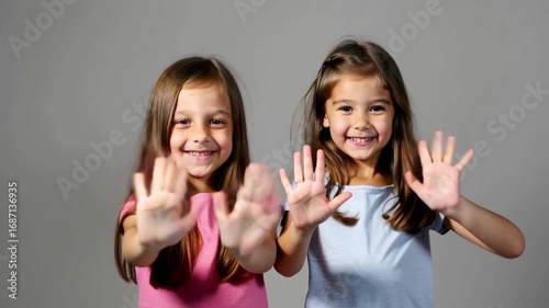 Joyful Children Two Young Girls Smiling, Waving, and Clapping in Casual Clothes Against Plain Background, Creating Cheerful Atmosphere of Happiness and Playful Interaction