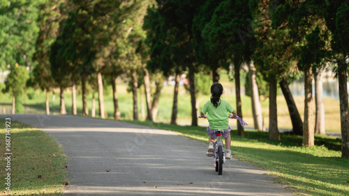 Wallpaper Mural Child Riding Bicycle on Pathway Surrounded by Lush Green Trees in a Serene Park Setting during Daytime Sunshine and Clear Blue Sky Torontodigital.ca