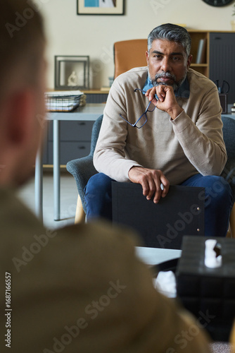 Картината върху платно Middle aged South Asian man sitting in office holding eyeglasses and clipboard l