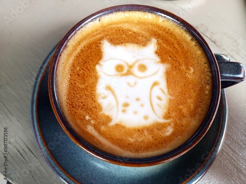 Cup of coffee on a table from above view and foam is shaped like a cute owl with glasses
