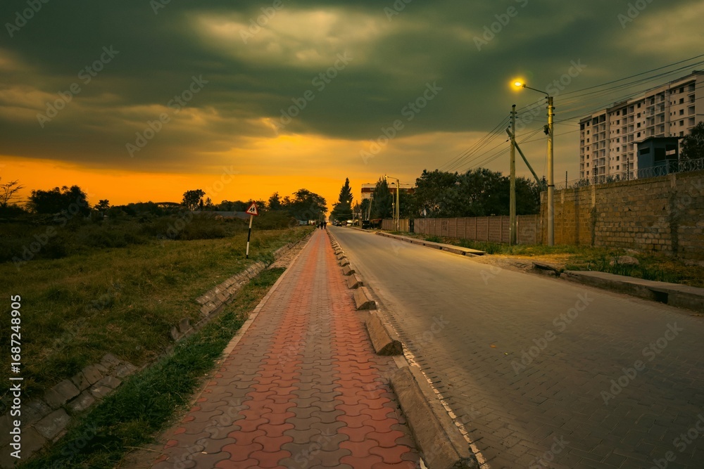 Obraz premium Scenic view of road amidst acacia trees and buildings against a golden sunset at Syokimau Suburb in Machakos County, Kenya 