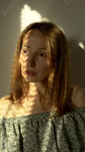 The female face of a white woman is illuminated by light and shadow in the room
