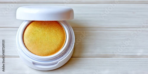 Round compact with golden shimmer makeup product, featuring a smooth texture, placed on a light wooden surface, showcasing beauty and cosmetic artistry in an elegant presentation