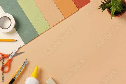 Supplies for paper art hobby: scissors, craft knife, pencil, eraser, colored paper on beige background. Space for your text.
