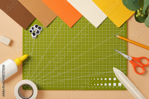 Green cutting mat surrounded by colored paper and crafting tools on a table. Creative workspace for arts and crafts.
