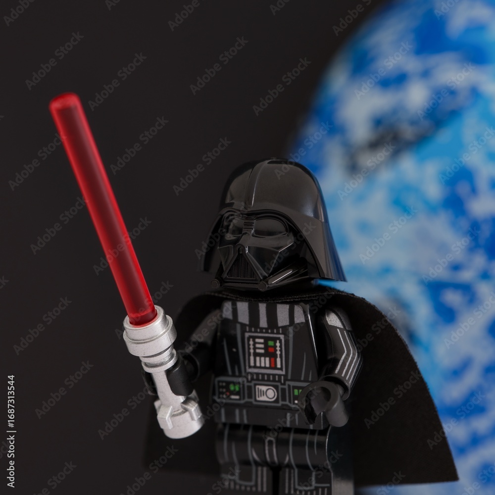 Fototapeta premium Tambov, Russian Federation - November 14, 2024 Lego Darth Vader minifigure with red lightsaber against black background with a blue planet