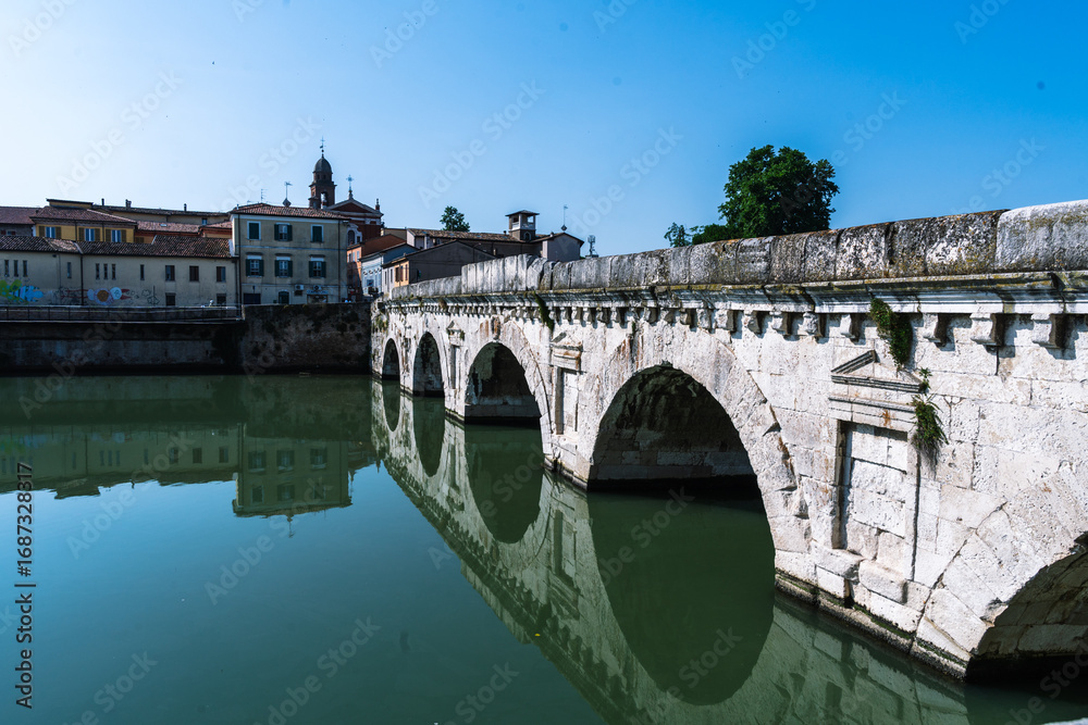 Fototapeta premium Ancient bridge over calm water, reflecting architecture and sky. A timeless landmark merges history with serene landscape.
