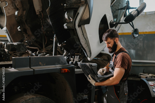 Mechanic using laptop diagnosing truck engine problem in garage