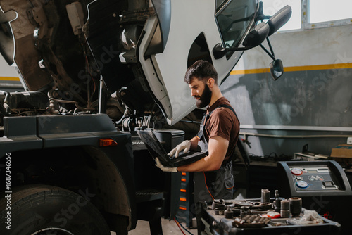 Fotografia Mechanic using laptop diagnosing truck malfunction in garage