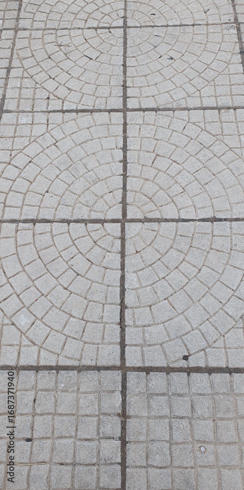 Obraz premium A top-down view of a city sidewalk with a geometric paving pattern of concentric circles. An abstract urban background for design, construction, and concepts of order.