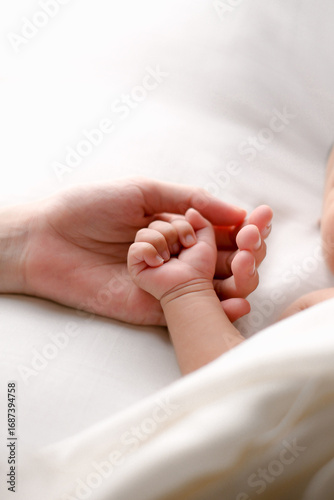 Close-up of a newborn baby’s hand gently holding a parent’s hand on a white sheet. Minimal, high-key image that symbolizes love, bonding, safety, and family care—ideal for parenting, maternity, health