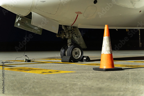 Airplane wheel on the runway waiting for takeoff, it is nighttime and the light is artificial. You can see some headsets on the ground that the coordinator uses to communicate with the pilot.