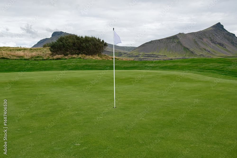 Obraz premium Scenic golf course with mountains, green field, and flag in Iceland countryside