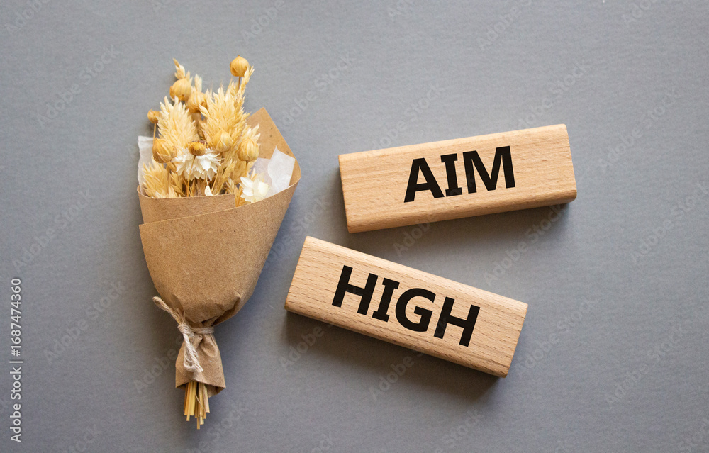 Aim High symbol. Wooden blocks with words Aim High. Beautiful grey background with bouquet of flowers. Business and Aim High concept. Copy space.