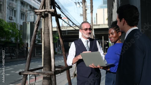 Business professionals having outdoor meeting on city street, discussing project with laptop, symbolizing teamwork, communication, leadership, consulting, and modern corporate strategy.