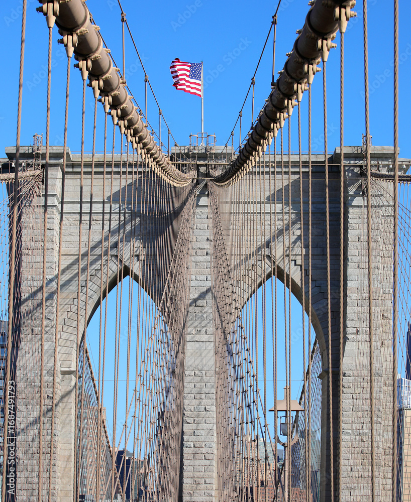 Fototapeta premium American Flag on the top of Brooklyn Bridge and steel cables in New York City in USA