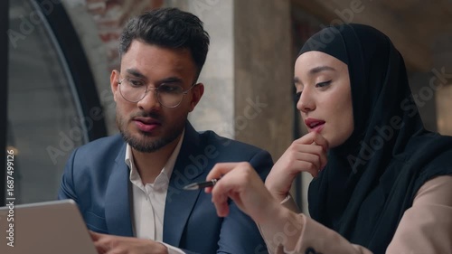 Muslim business team two managers man woman looking laptop discuss project startup brainstorming Islamic businesswoman in hijab Indian businessman working together communicate negotiate in office