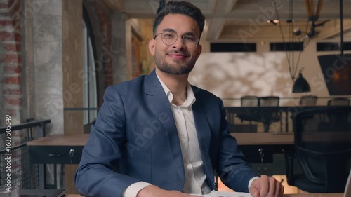 Pensive Indian business man working with papers businessman smiling in camera nodding head yes satisfied in office Arabian ethnic guy male specialist writing documents information with laptop happy