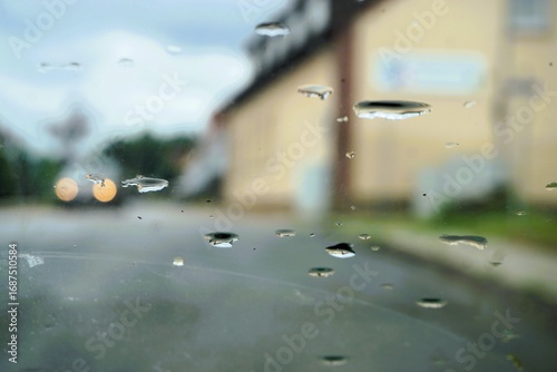Abstraktes Motiv mit Auto mit goldenen Lichtern auf Straße neben Gebäude in Kleinstadt bei regen am Nachmittag im Sommer