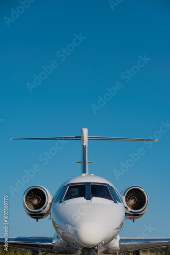 Head-on view of a business jet showing cockpit windows, twin turbo fan engine and the tail. Top of the image is clear sky with ample copy space.