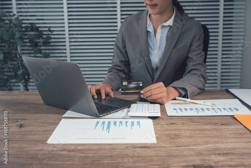 Fotografie Focused Professional at Work: An accomplished professional, fully engrossed in her work, meticulously reviews data and engages with a laptop on her desk, surrounded by financial documents